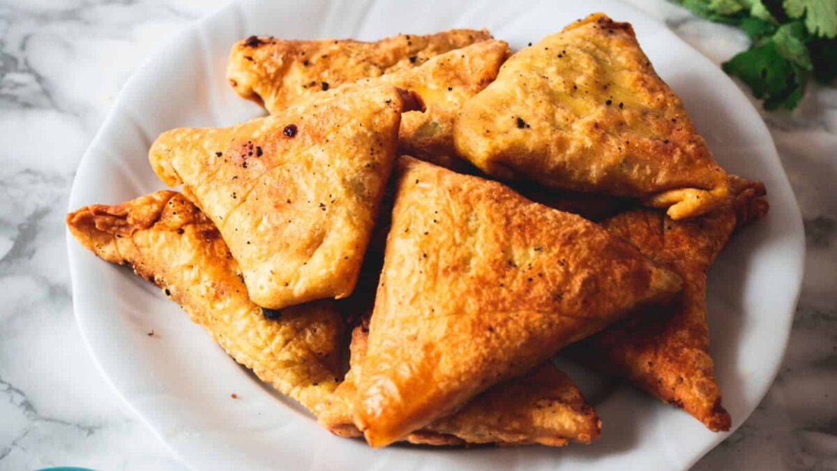 A white plate filled with several golden-brown, triangular fried pastries on a marble surface—perfect for those seeking unique snacks or new snack ideas.