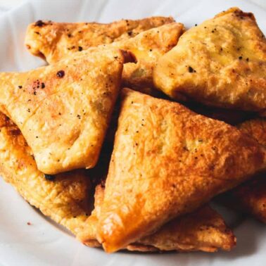 A white plate filled with several golden-brown, triangular fried pastries on a marble surface—perfect for those seeking unique snacks or new snack ideas.