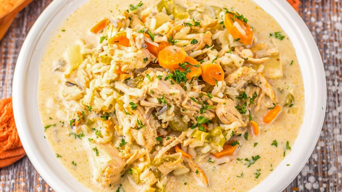 A bowl of creamy chicken and rice soup with carrots, celery, and herbs, served in a white bowl on a wooden surface—one of the best easy meals for cozy nights and perfect for fans of slow cooker recipes.