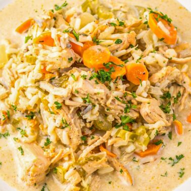 A bowl of creamy chicken and rice soup with carrots, celery, and herbs, served in a white bowl on a wooden surface—one of the best easy meals for cozy nights and perfect for fans of slow cooker recipes.