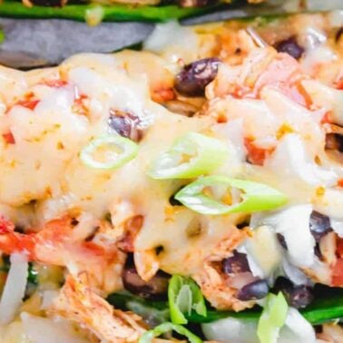 Close-up of stuffed jalapeños filled with melted cheese, black beans, shredded chicken, tomatoes, and topped with sliced green onions—the smell evokes pure happiness.