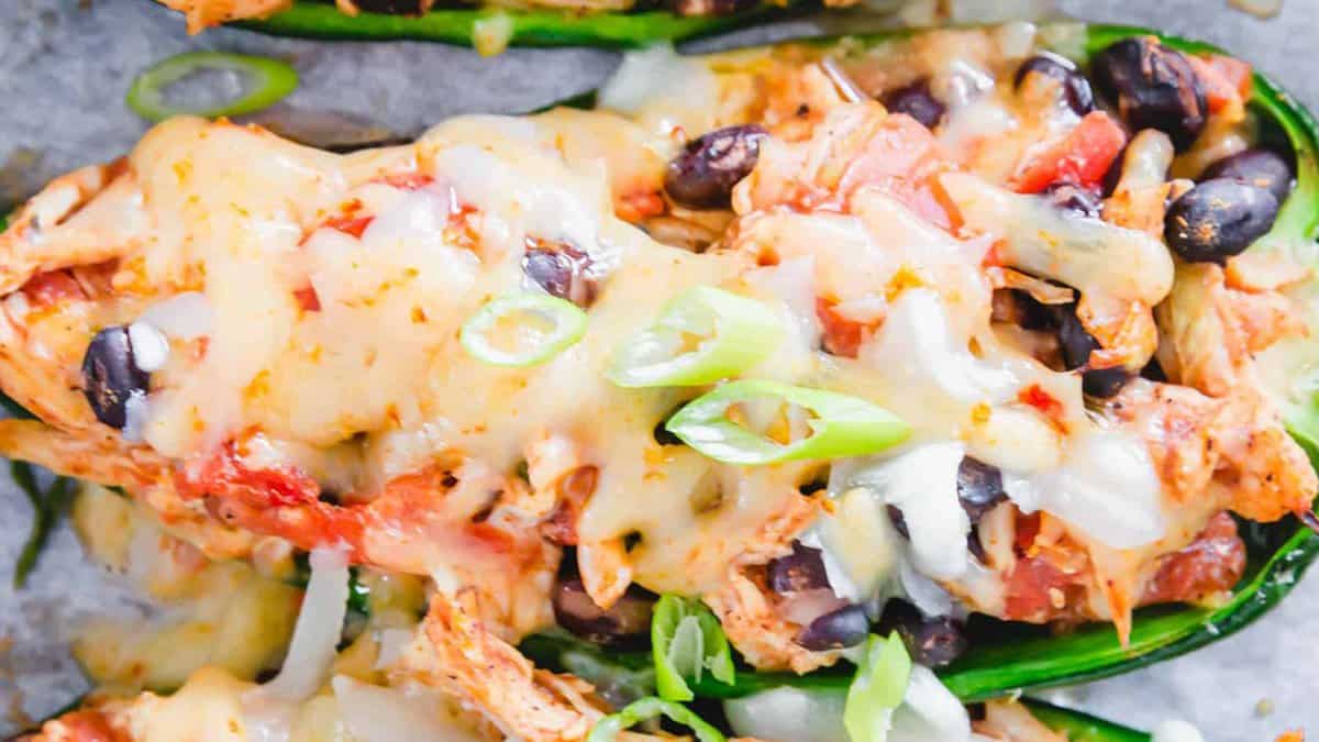 Close-up of stuffed jalapeños filled with melted cheese, black beans, shredded chicken, tomatoes, and topped with sliced green onions—the smell evokes pure happiness.