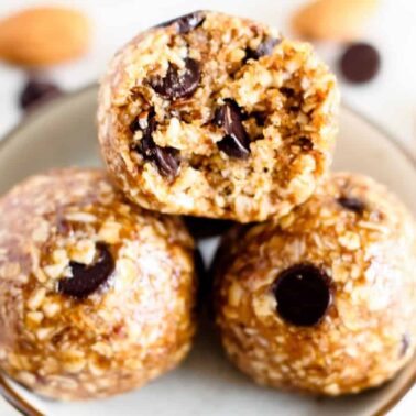 A close-up of three plant-based snacks featuring oats and chocolate chips in a bowl, surrounded by almonds and more chocolate chips.