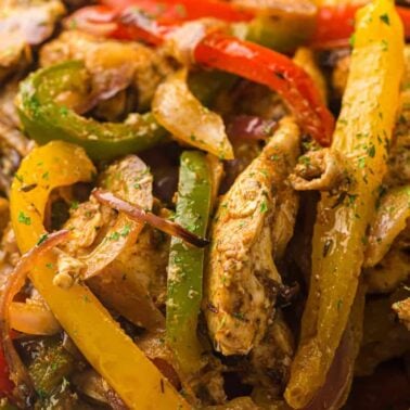 Close-up of cooked chicken strips mixed with sautéed red, yellow, and green bell peppers and onions, seasoned with herbs—perfect for crunchy recipes or as a delicious addition to your favorite air fryer recipes.