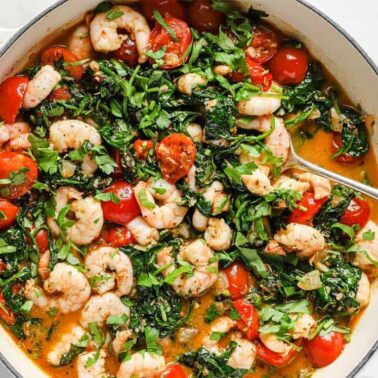 Shrimp sautéed with cherry tomatoes, spinach, herbs, and a light sauce in a white pan—a perfect seafood dinner after long beach days, served with a spoon on the side.