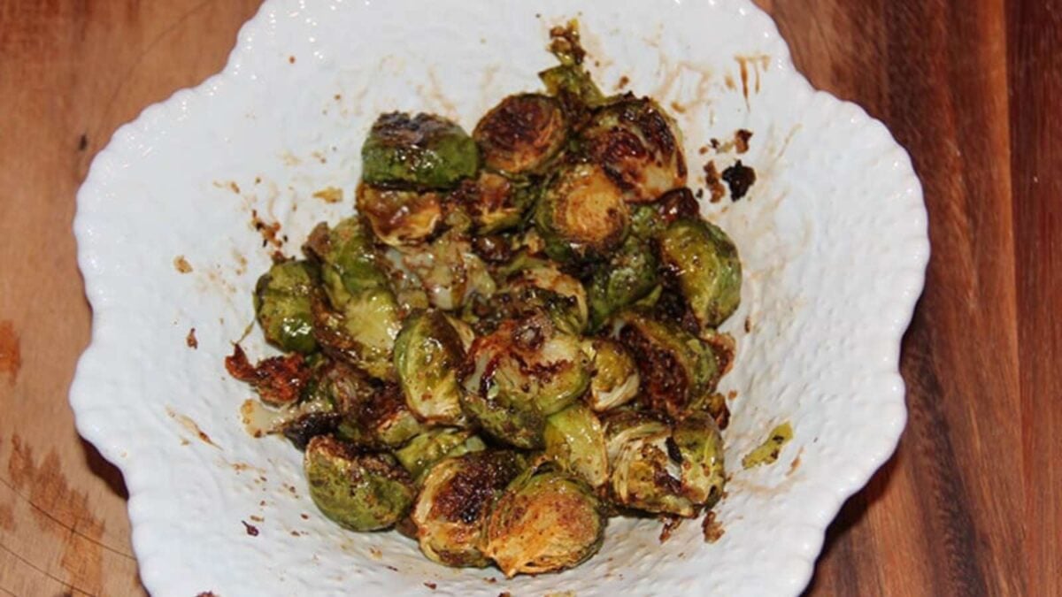 Roasted Brussels sprouts with browned, crispy edges served in a white textured bowl on a wooden surface—one of the best side dishes to complement any meal.