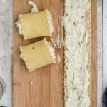 Two rolled lasagna noodles and one unrolled noodle with cheese filling on a wooden cutting board, viewed from above.
