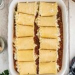 A white baking dish filled with rolled lasagna noodles placed on top of a layer of meat sauce, ready to be baked.