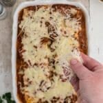 A person holding cheese over a casserole.