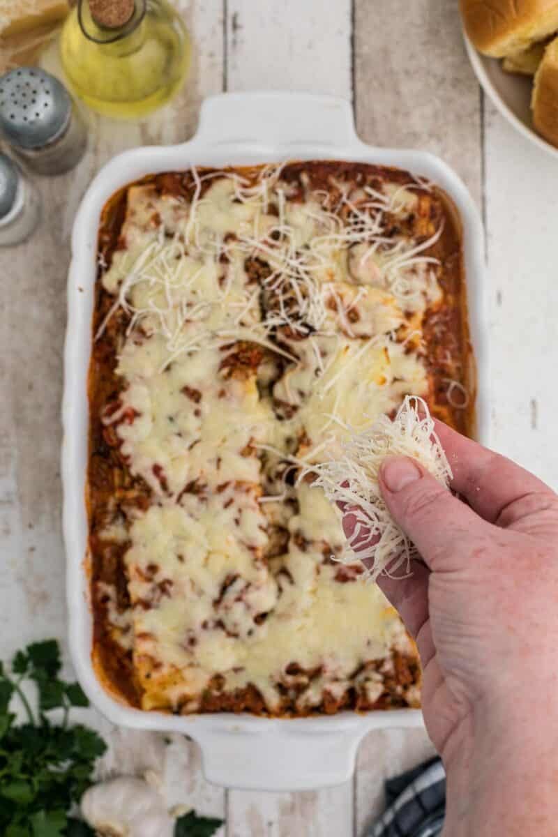 A person holding cheese over a casserole.