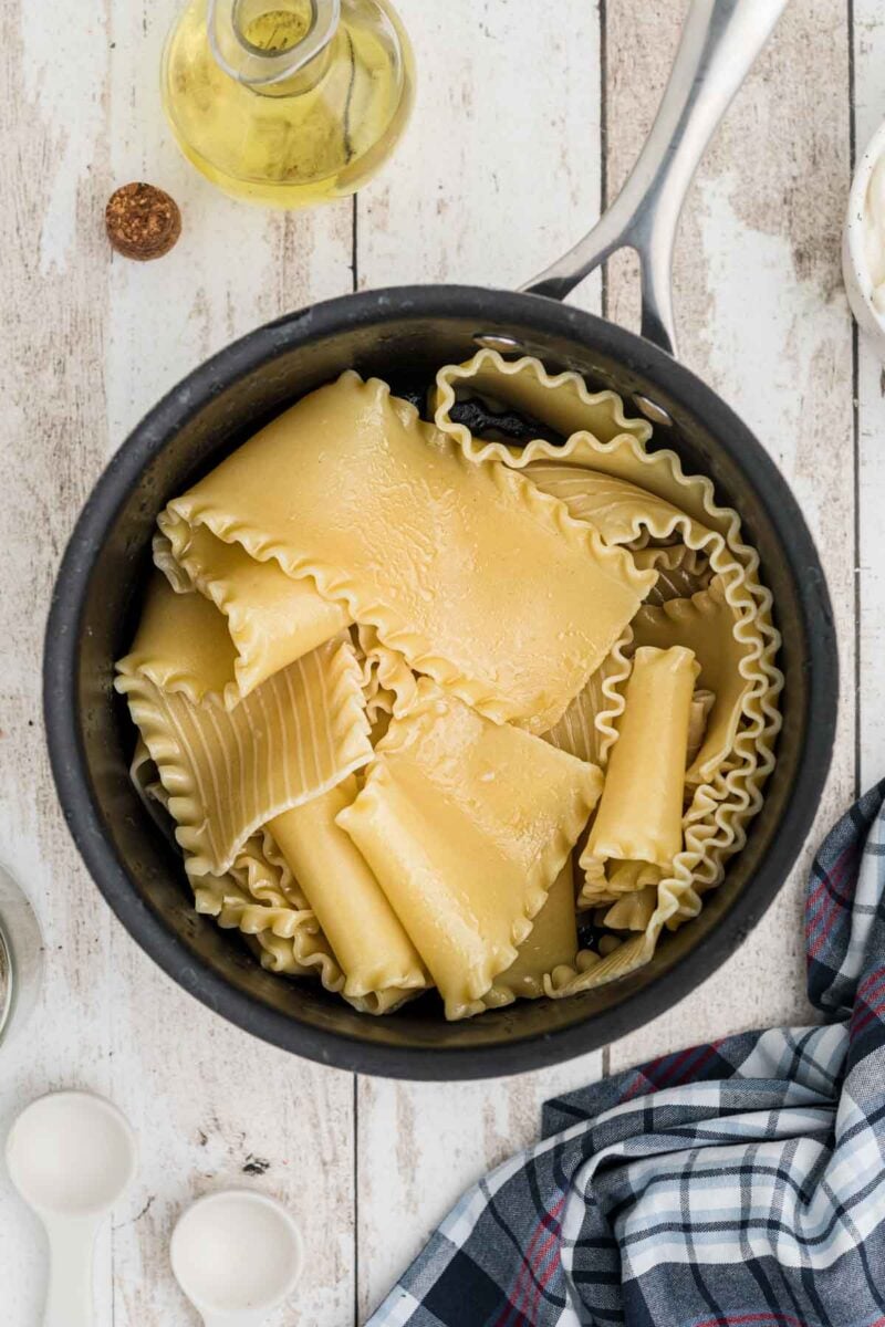 A pot of pasta with a towel and a towel on a white wood surface.