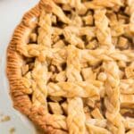 A close-up of a baked salted caramel apple pie with a golden brown, braided lattice crust in a white pie dish.