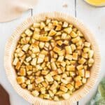 Unbaked pie crust filled with chopped apples and brown sugar mixture on a white surface, with rolled dough, melted butter, and a green apple nearby.
