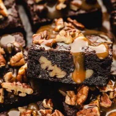 Close-up of turtle chocolate brownies topped with pecans and drizzled with caramel sauce.