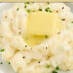 A plate of mashed potatoes topped with a pat of butter and chopped chives, sprinkled with black pepper. Text reads "13 Mashed Potatoes Are Creamy and Comforting.