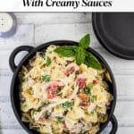 A bowl of creamy bow-tie pasta with chicken, tomatoes, and herbs sits on a white wooden table, garnished with fresh basil.