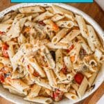 Bowl of penne pasta with vegetables and herbs, topped with sauce, on a wooden board. Text overlay reads "14 Pastas That Wake Up Weeknights.