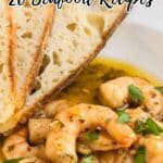 Cooked shrimp in a herb sauce served with two slices of rustic bread on a white plate; overlaid text reads “20 Seafood Recipes.”.