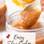 A spoon scoops apple butter from a glass jar. Text overlay reads: "Easy Slow Cooker Apple Butter." Another jar and autumn leaves are in the background.