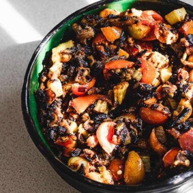 A green and black bowl filled with charred and roasted vegetables, including tomatoes and zucchini, sits on a light countertop—perfect inspiration for vegan recipes.