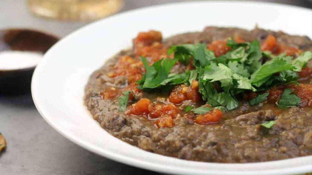 A white plate filled with refried black beans, topped with chopped tomatoes and fresh cilantro—perfect for cozy fall recipes.