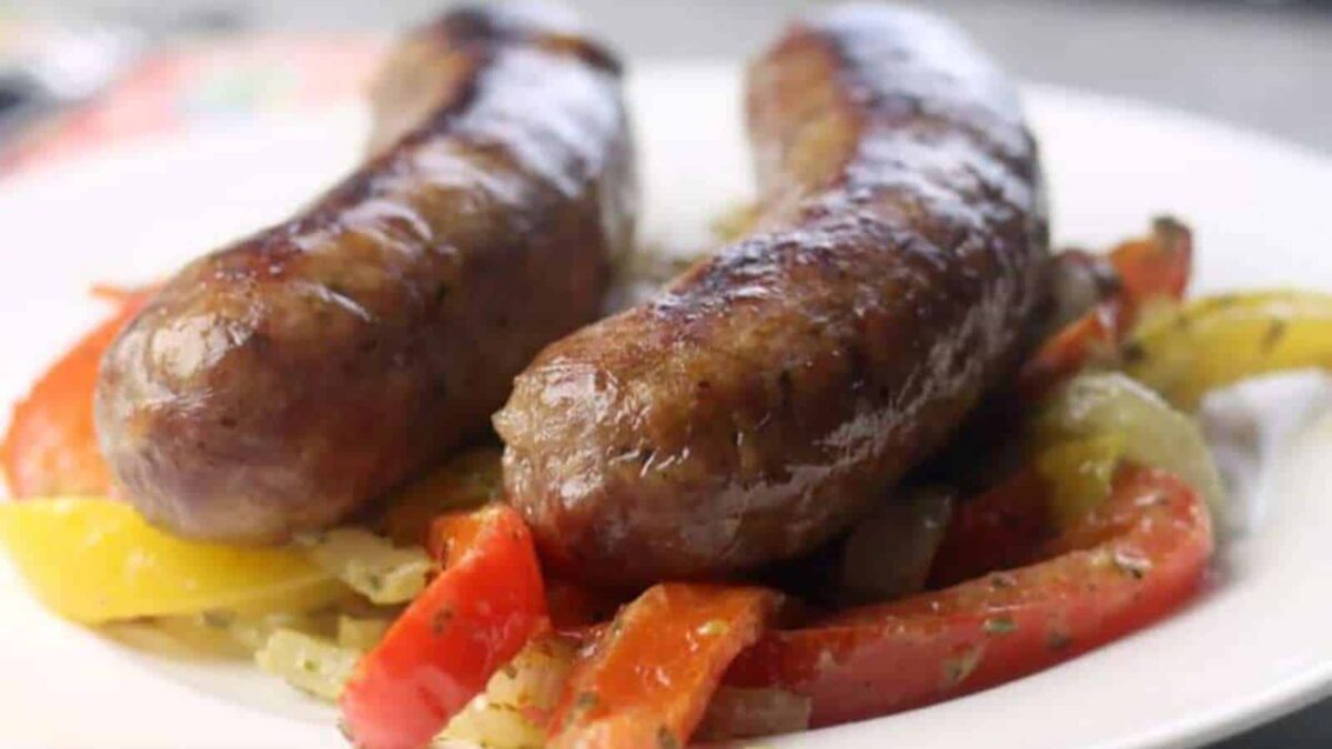 Two grilled sausages served on a bed of sautéed red and yellow bell peppers and onions on a white plate—a colorful addition to your collection of bold sausage recipes.