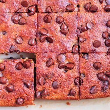 Close-up of chocolate chip blondies, freshly baked and cut into squares on parchment paper, with one piece slightly pulled out—perfect for anyone who loves homemade baked goods.