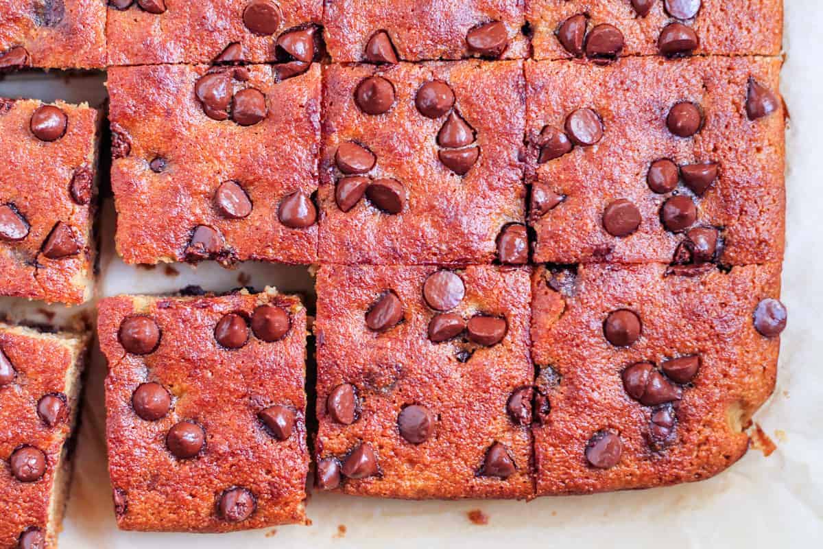 Close-up of chocolate chip blondies, freshly baked and cut into squares on parchment paper, with one piece slightly pulled out—perfect for anyone who loves homemade baked goods.