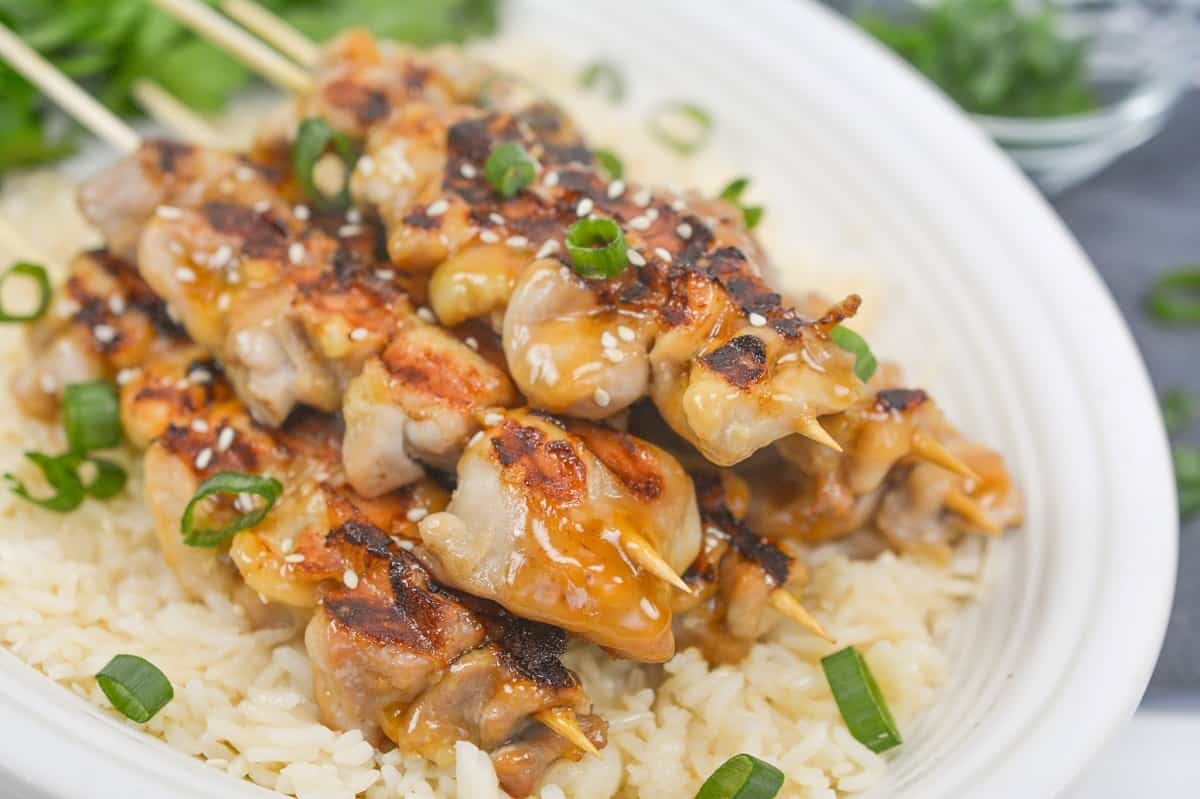 Grilled chicken skewers with sauce and sesame seeds served over steamed rice, garnished with chopped green onions—one of our favorite quick recipes for easy dinners.