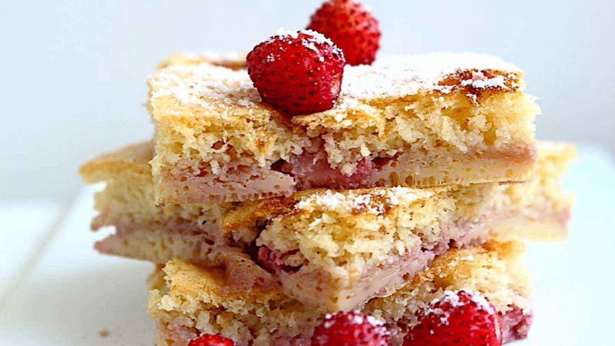 Three stacked pieces of strawberry cake, reminiscent of home baking, are topped with whole strawberries and dusted with powdered sugar.