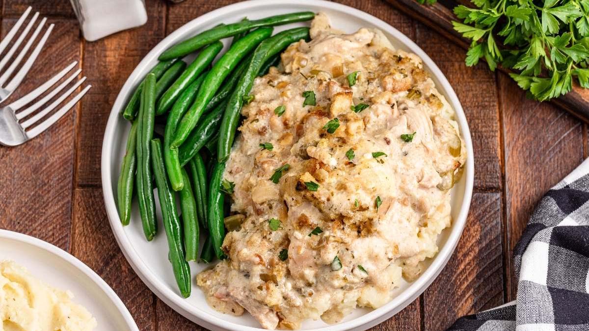 A plate of green beans served alongside a creamy chicken casserole topped with herbs, placed on a wooden table with parsley and a fork nearby—perfect inspiration for easy stuffing recipes at your next holiday meal.