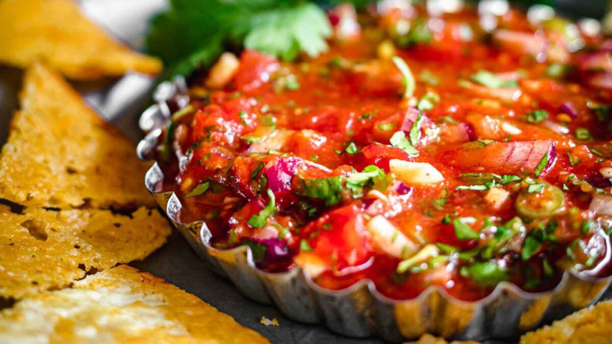 A close-up of fresh salsa with chopped vegetables in a metal dish, surrounded by tortilla chips—one of the most irresistible side dishes for any gathering.