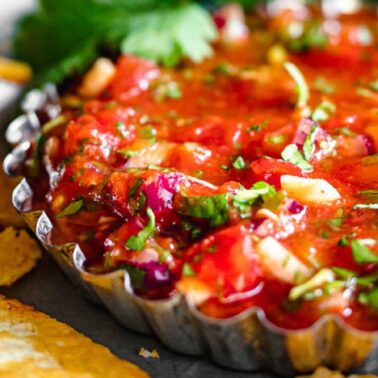 A close-up of fresh salsa with chopped vegetables in a metal dish, surrounded by tortilla chips—one of the most irresistible side dishes for any gathering.