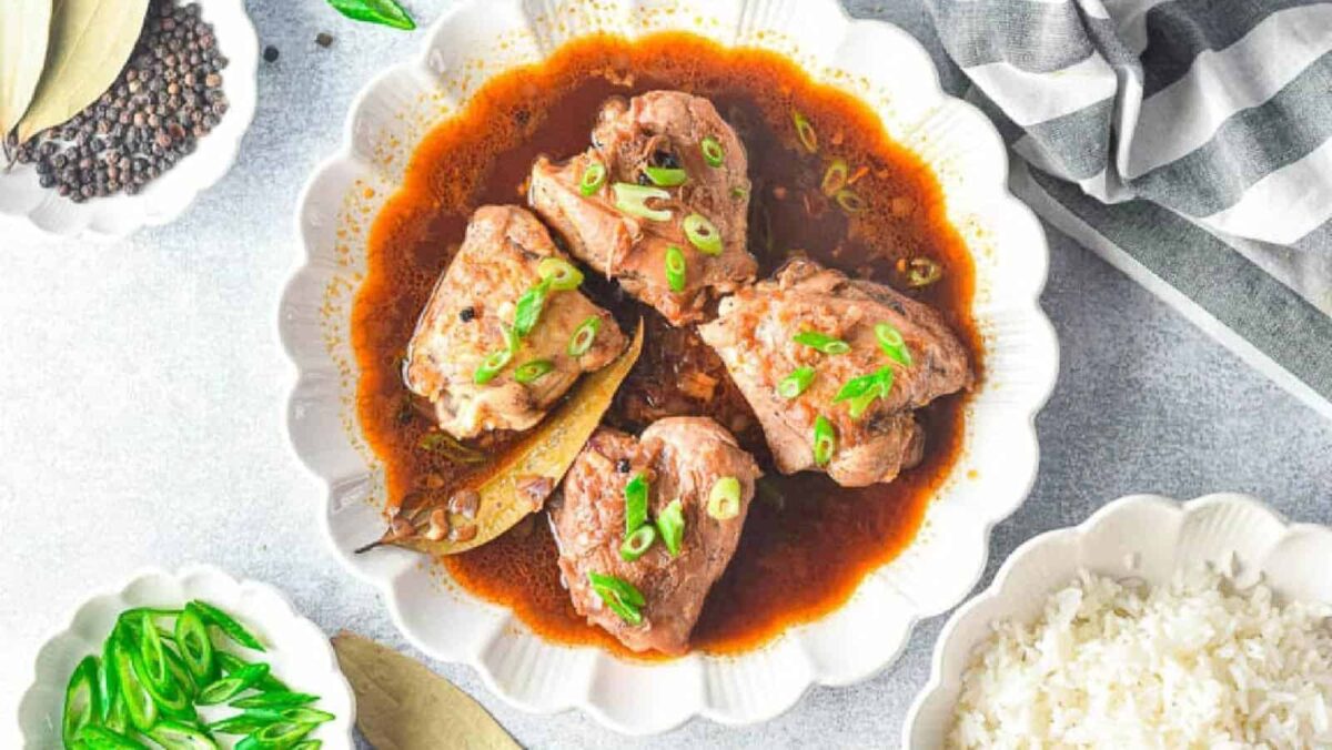 A bowl of braised meat in brown sauce garnished with chopped green onions, accompanied by rice, green chilies, bay leaves, and black peppercorns—perfect comfort food for easy dinner recipes.