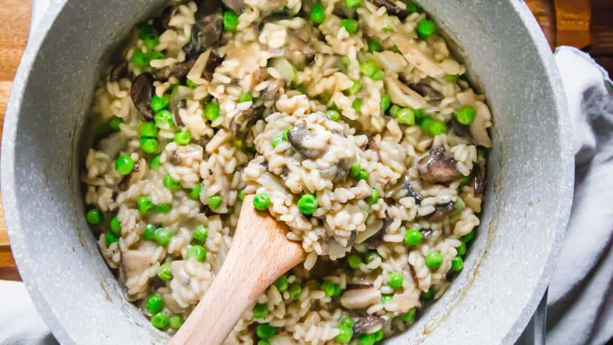A pot of mushroom and pea risotto with a wooden spoon stirring the creamy rice mixture—perfect for comfort dinners.