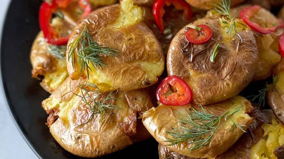 A plate of smashed roasted potatoes garnished with red chili slices and fresh herbs—a must-try for fans of creative potato recipes.