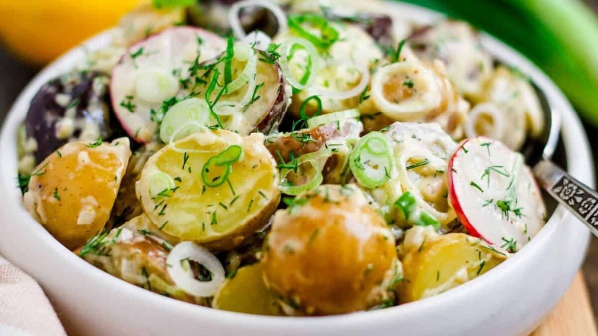 A bowl of potato salad with sliced radishes, chopped green onions, and fresh dill, dressed in a creamy sauce—one of those unique potato dishes that's perfect for anyone seeking easy potato meals.