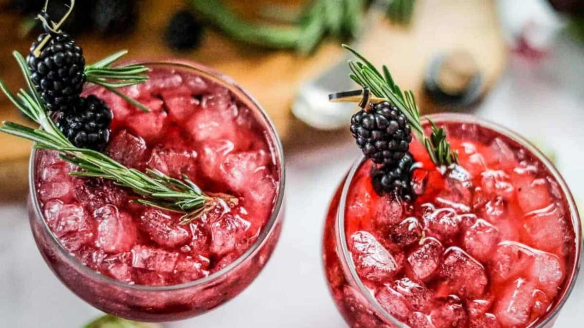Two glasses filled with crushed ice and a red beverage, garnished with fresh blackberries and rosemary sprigs—an inviting scene perfect for fans of berry dishes or those seeking inspiration for flavorful desserts.