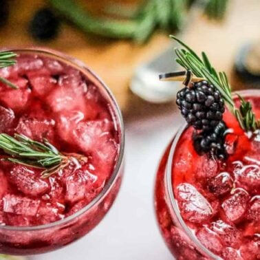 Two glasses filled with crushed ice and a red beverage, garnished with fresh blackberries and rosemary sprigs—an inviting scene perfect for fans of berry dishes or those seeking inspiration for flavorful desserts.