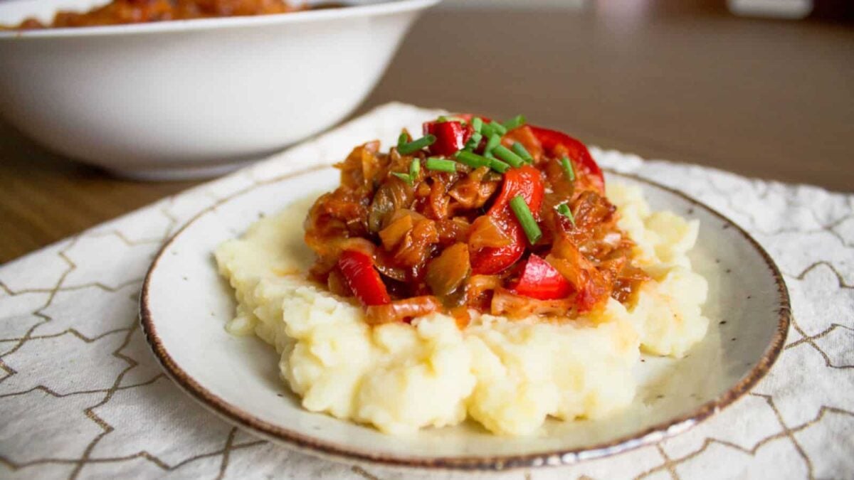 A plate of mashed potatoes topped with a hearty vegetable stew and garnished with chopped chives sits on a patterned napkin—perfect inspiration for healthy sides and delicious veggie side dishes.