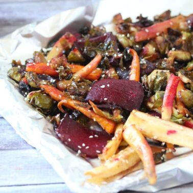 A tray of roasted root vegetables, including carrots, parsnips, Brussels sprouts, and beets, garnished with sesame seeds on a sheet of foil—perfect for those seeking delicious and healthy side dishes.