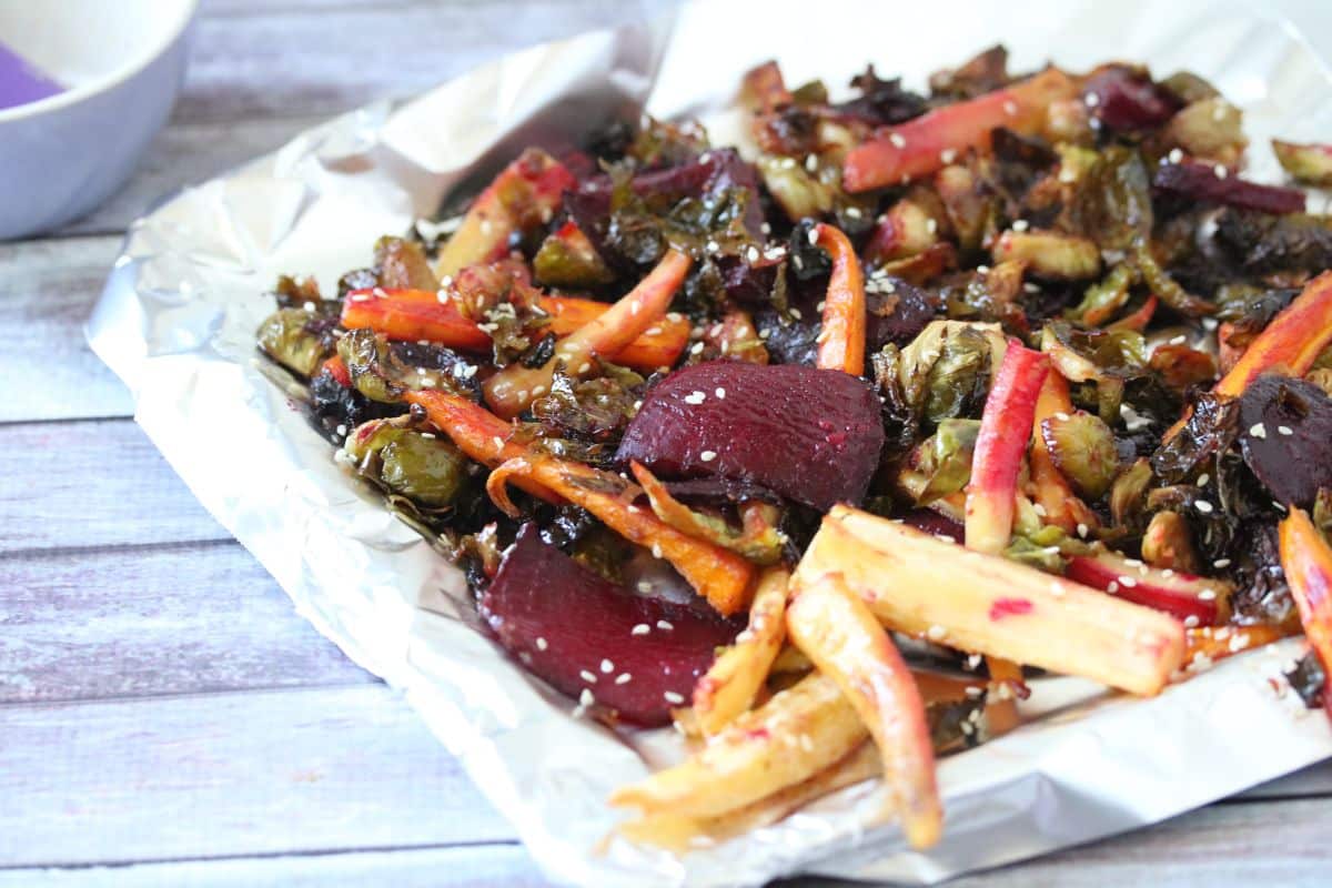 A tray of roasted root vegetables, including carrots, parsnips, Brussels sprouts, and beets, garnished with sesame seeds on a sheet of foil—perfect for those seeking delicious and healthy side dishes.