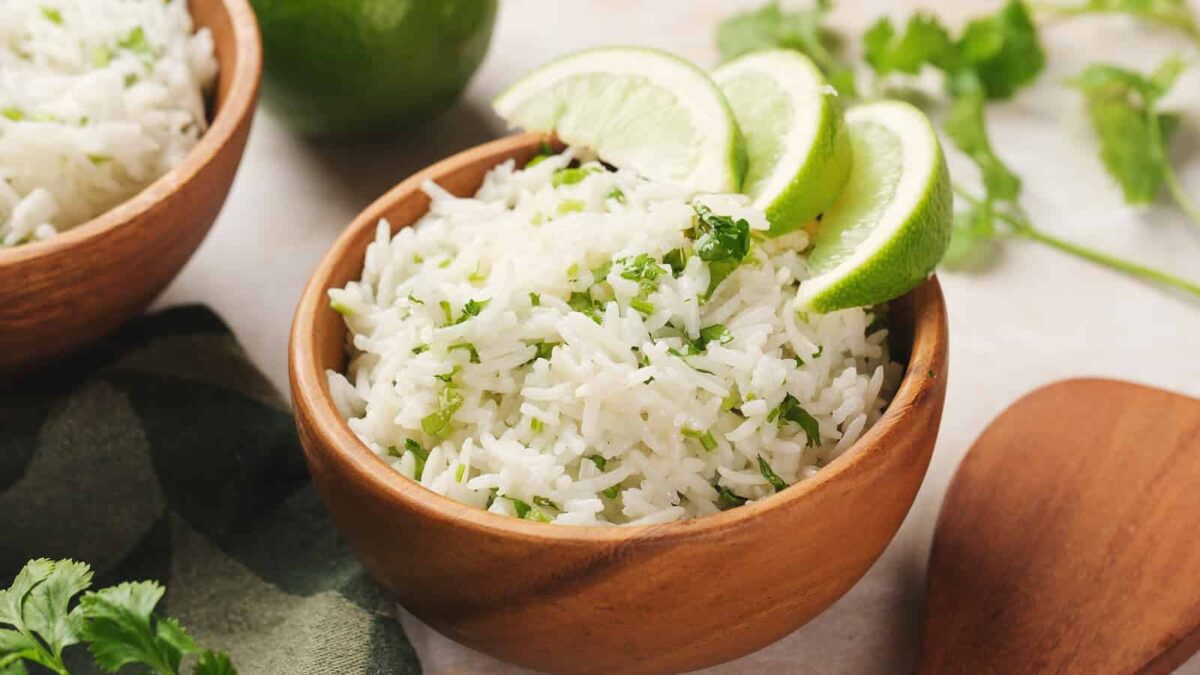 A wooden bowl filled with white cilantro-lime rice, garnished with lime wedges. Perfect for fans of rice dishes, with fresh cilantro and a lime in the background.