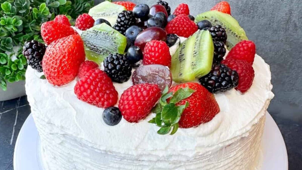 A round morning cake with white frosting, topped with strawberries, raspberries, blackberries, blueberries, grapes, and sliced kiwi fruit.