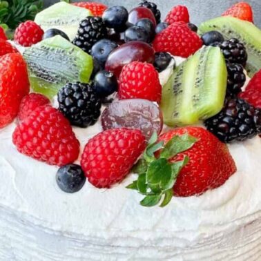 A round morning cake with white frosting, topped with strawberries, raspberries, blackberries, blueberries, grapes, and sliced kiwi fruit.