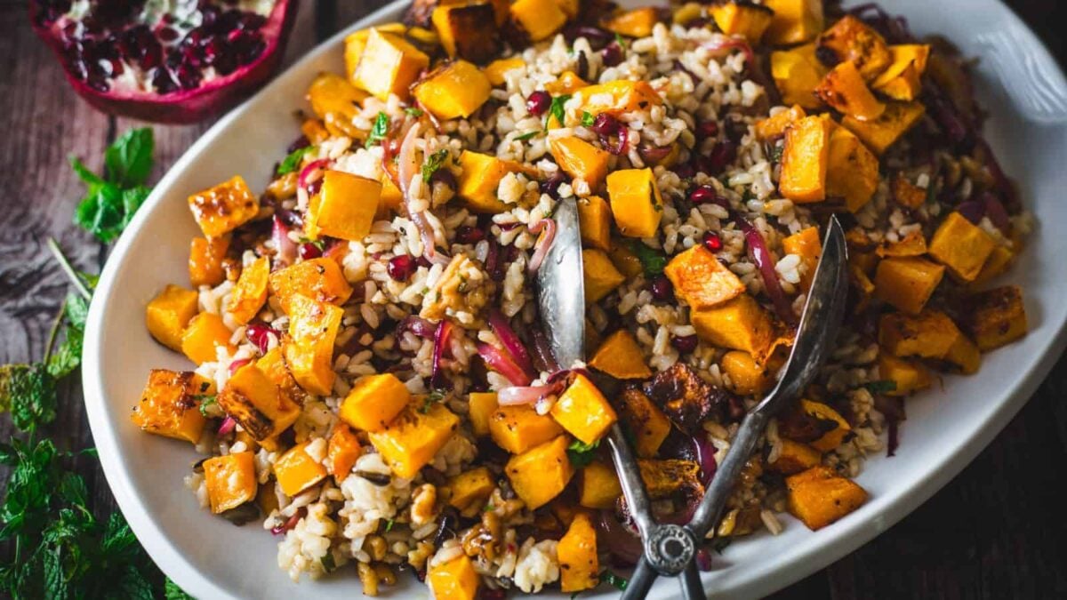 A serving platter with a vibrant mixed rice salad, roasted butternut squash cubes, red onions, walnuts, and fresh herbs—showcasing how rice bowl recipes can come together easily with simple ingredients. Includes a pair of serving tongs.