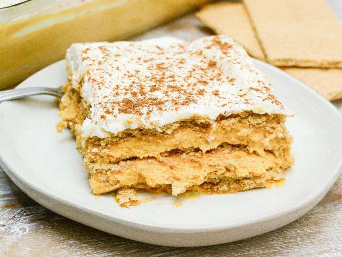 A slice of layered pumpkin dessert topped with whipped cream and sprinkled with cinnamon, served on a white plate—one of our delicious nut free desserts perfect for allergy friendly snacks.