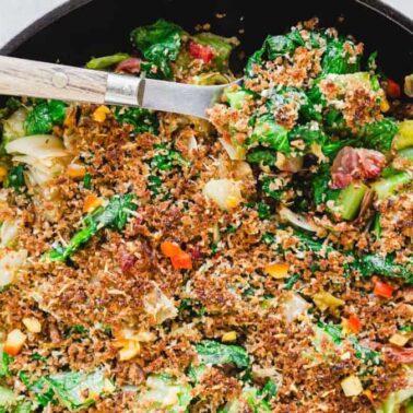 A cast iron skillet filled with a baked vegetable casserole topped with golden toasted breadcrumbs, making it perfect for side dishes or as a hearty main course, with a serving spoon placed inside.