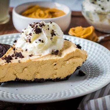 A slice of peanut butter pie with Oreo crust, topped with whipped cream and cookie crumbs, served on a white plate with Oreo cookies—a magical dessert perfect for those who crave decadent treats.