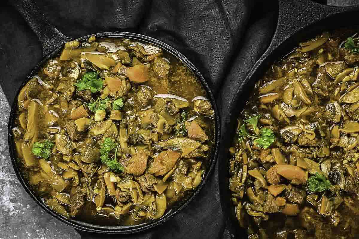 Two cast iron skillets filled with a hearty stew featuring beef, carrots, mushrooms, and fresh parsley—perfect for those who love classic beef recipes.